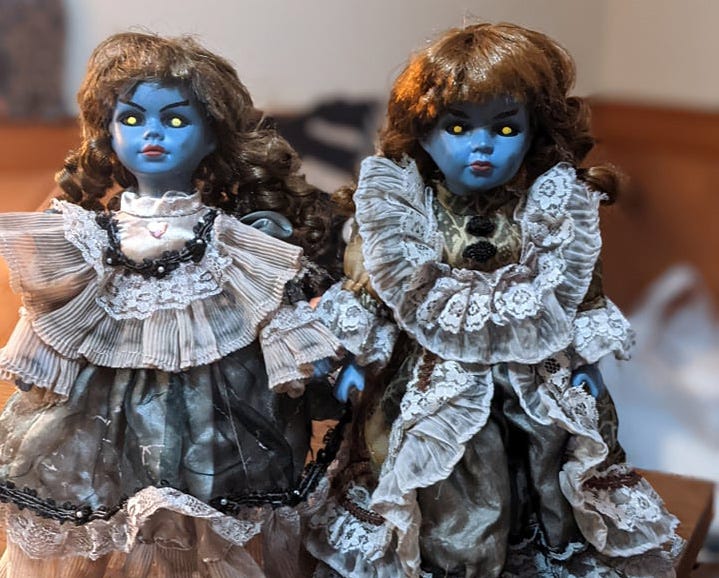 Two creepy dolls with blue faces and glowing yellow eyes. Two creepy dolls with blue faces and glowing yellow eyes.