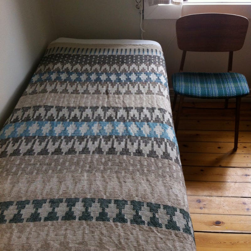 Handwoven blanket on single bed, with chair next to bed
