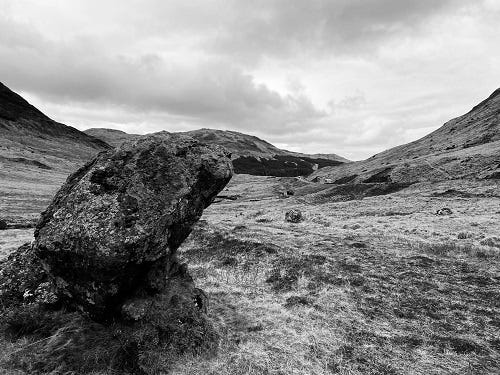 wide valley where the short dry grass os scattered with boulders. A large boulder in the foreground