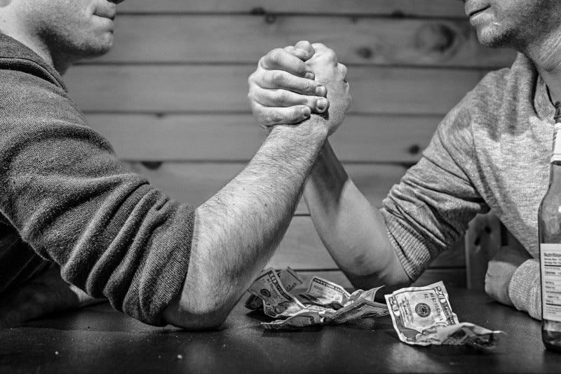 two men arm wrestling with money on the table