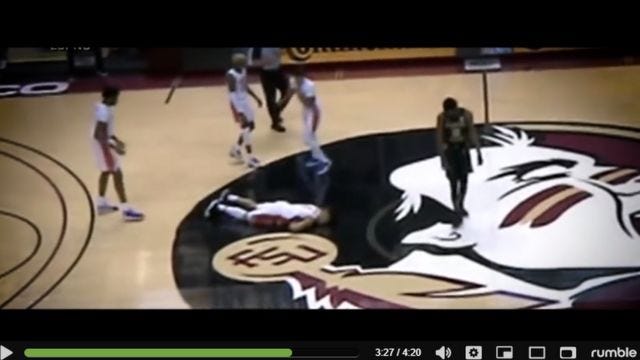 screenshot from video of basketball player face-down on floor with team mates surrounding him