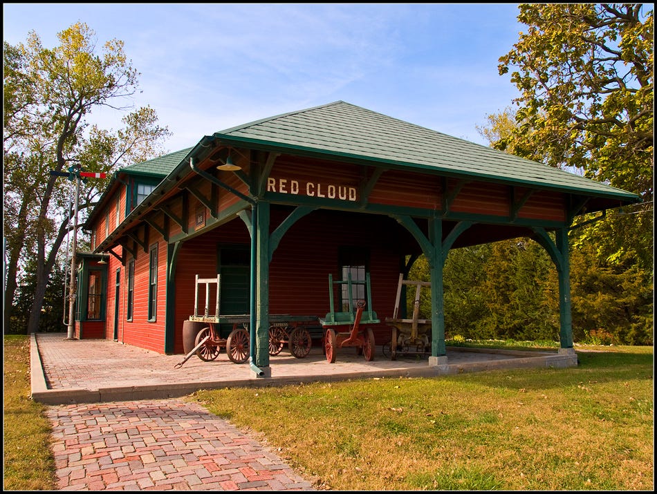 A railroad depot in Red Cloud Nebraska, brick sidewalk, green roof, red clapboard walls