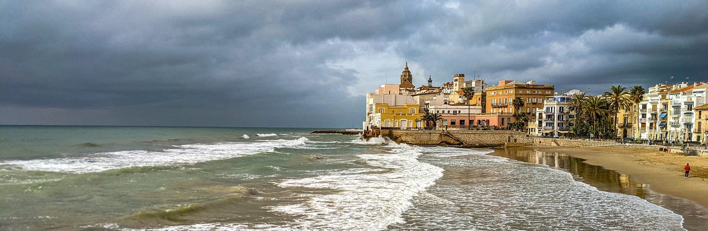The town of Sitges as seen from the north showing waves rolling in under dark grey skies.