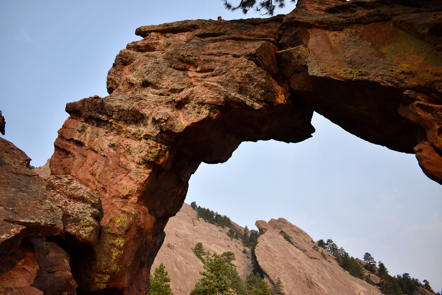 a climber looks down from atop an arched rock formation.