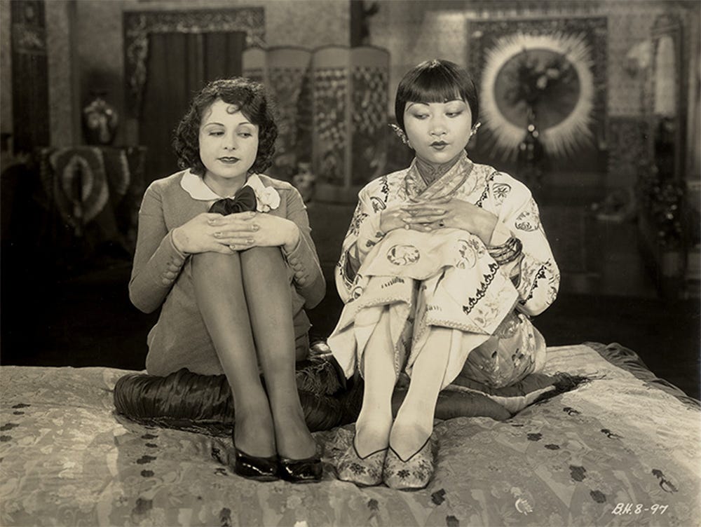 a black and white photo of actresses Louise Lorraine and Anna May Wong sitting with their hands folded on their knees, for the film Chinatown Charlie (1928)