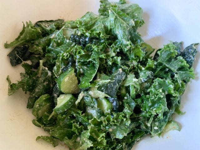 A green salad with leafy kale and pieces of cucumber