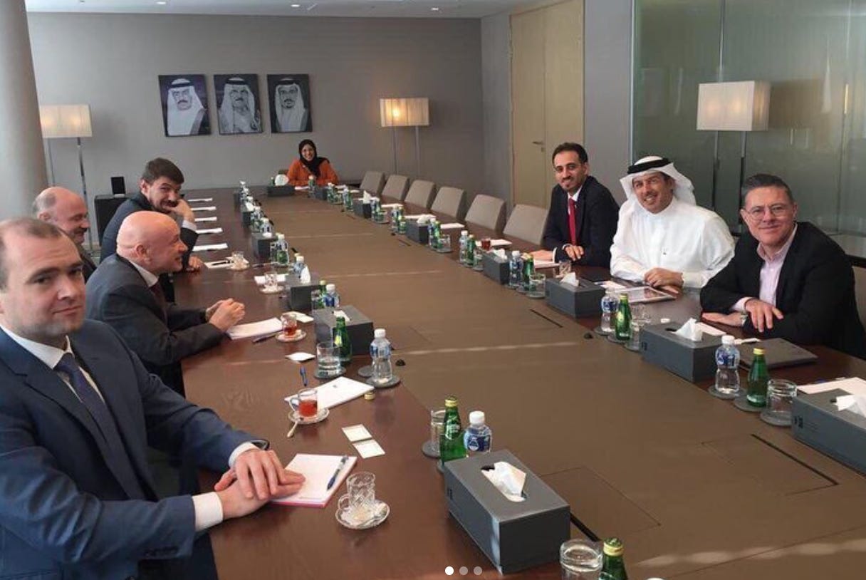 The Technotech deputy general manager Yaroslav Zhulanov (person on the far left of the image in a blue suit and blue tie) is pictured on a visit to the Kingdom of Bahrain in 2019, alongside other members of the Moscow Chamber of Commerce. The business meeting is occurring in a modern furnished conference room with white walls and light fixtures on the ceiling and in the corners of the room. At the center of the photo, a long table with eight people sitting around the table. Some are in Western business wear such as suit and ties, one person at the far end of the table wears an abaya and hijab, and one person on the right hand side of the table wears a thobe and ghitraa. There are some empty seats on the conference table. Each place at the table, whether occupied or empty, is set with a box of tissues, a plastic water bottle, and a glass bottle of mineral water. Each person has in front of them on the table also a clear cup of black tea on a saucer. On the wall behind the conference table are three frames with large photos of the rulers of Bahrain such as Hamad bin Isa Al Khalifa.