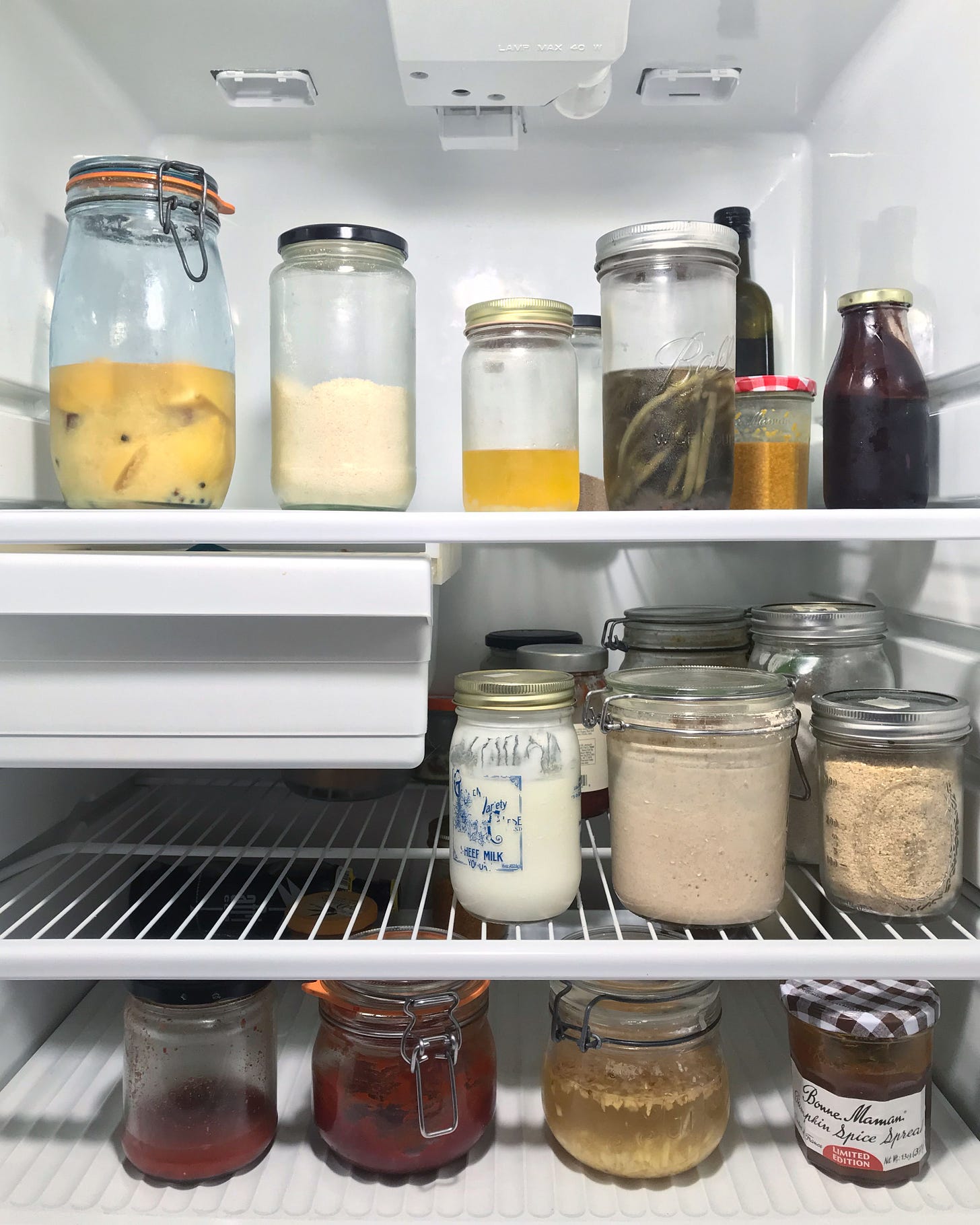3 shelves in a refrigerator, filled with clear glass jars of various kinds of food