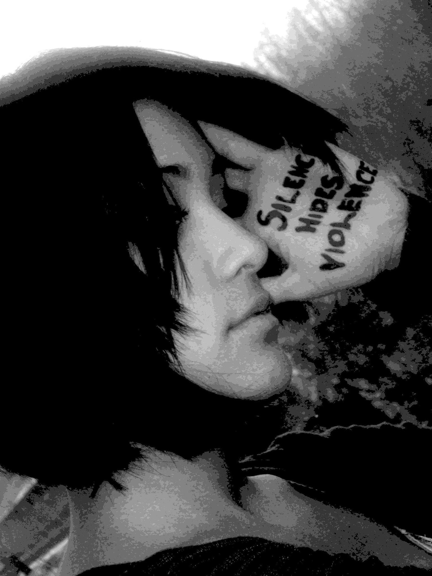 Young woman with hand to her head and the words "Silence hides violence" written on her palm