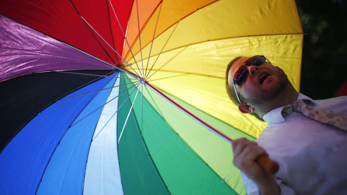 a man in a tie holding a rainbow umbrella 