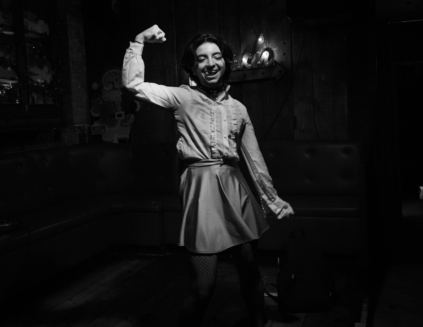 b&w photo of drag performer Peach Bellini smiling and holding up arm to flex bicep muscle