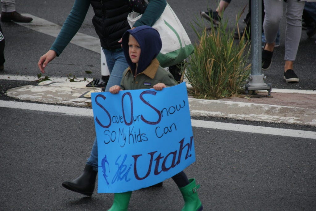 A child carries a sign that reads, Save our snow so my kids can ski Utah!