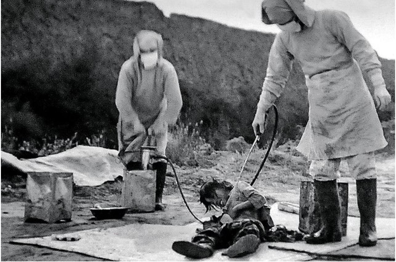 Two Japanese members of Unit 731 in hazard suits spray a bacteriological substance through a hose on a Chinese test victim.