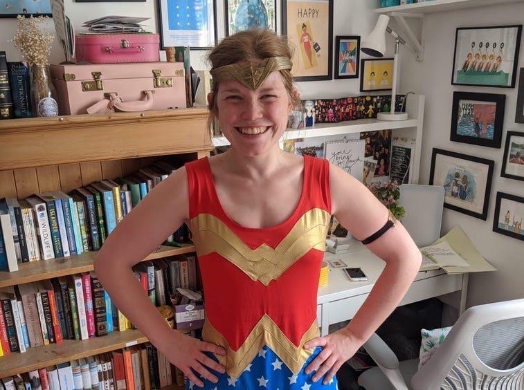 Libby standing in her office dressed in a Super Woman outfit