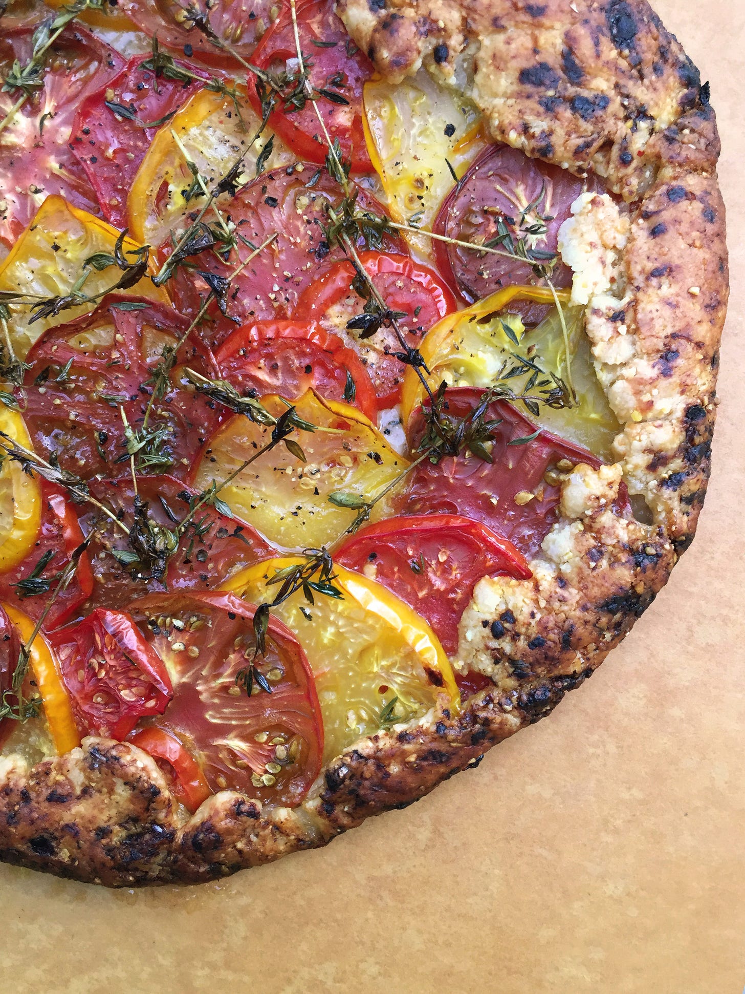 in a pastry crust with browned edges, three colours of heirloom tomato slices overlap each other. On top are several caramelized sprigs of thyme, and a dusting of black pepper.