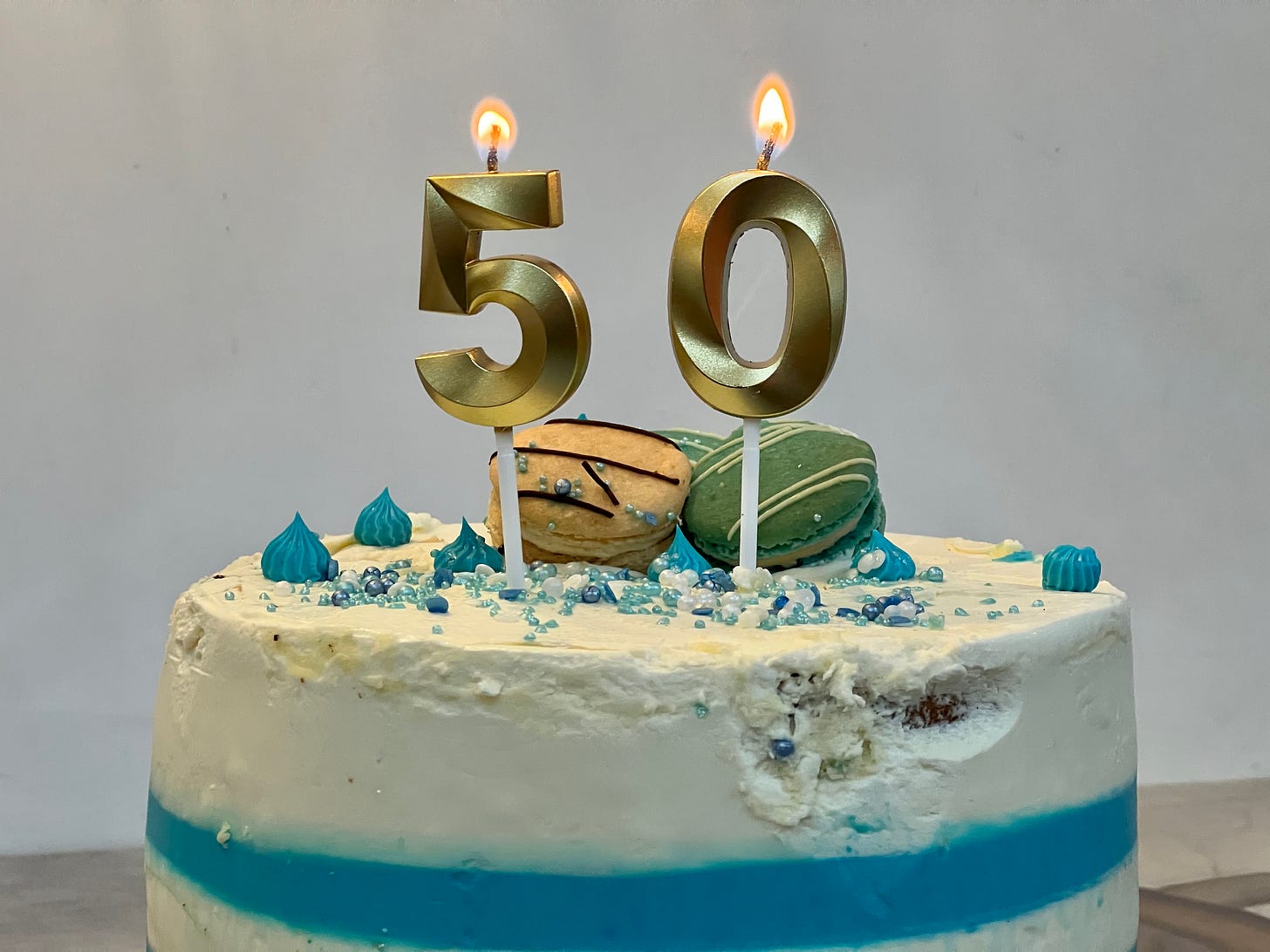 Two candles in the shape of numbers five and zero are lit above a creamy cake with fancy macaroons on top. 