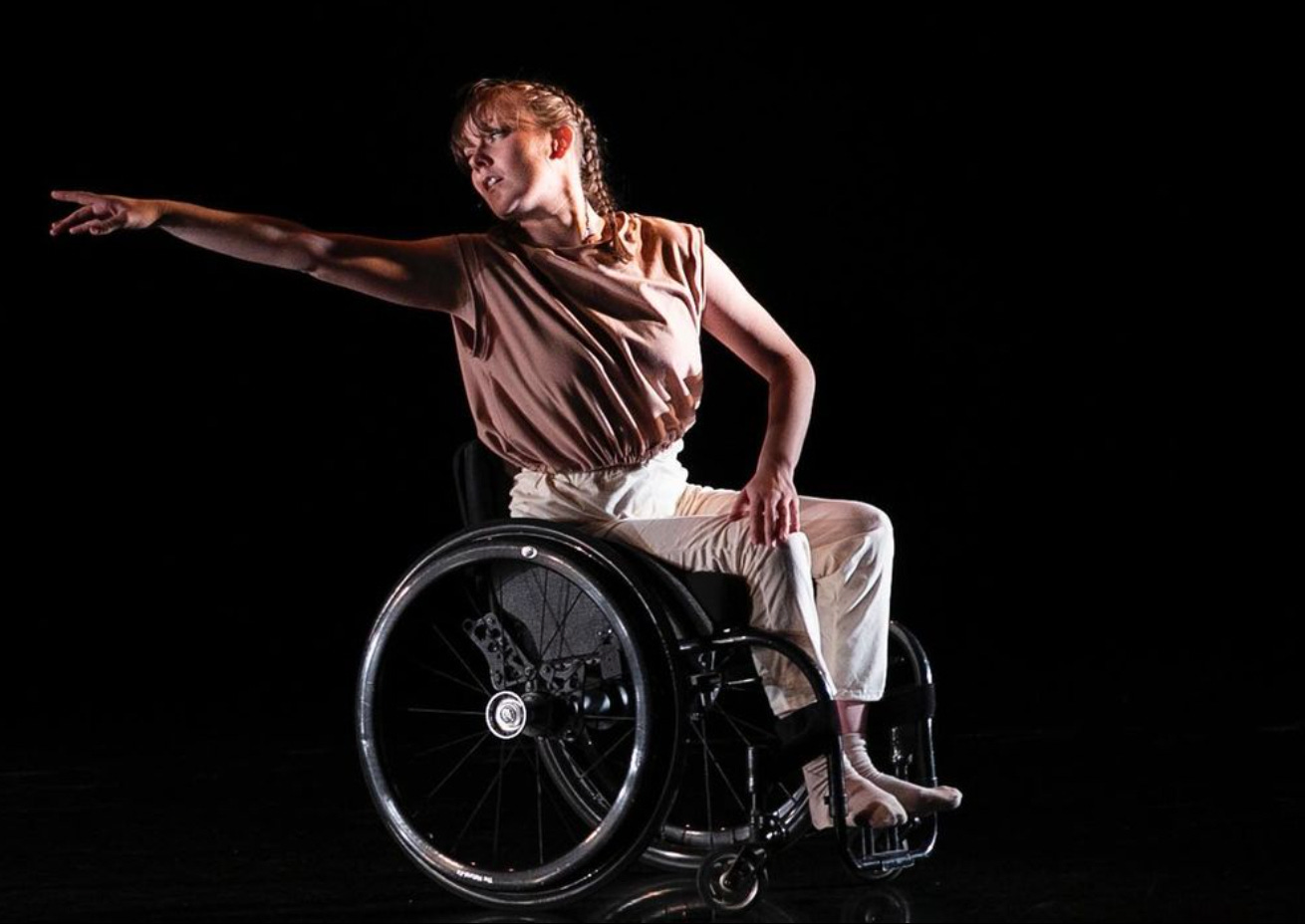white wheelchair dancer with french braids reaches and gazes behind them in the distance