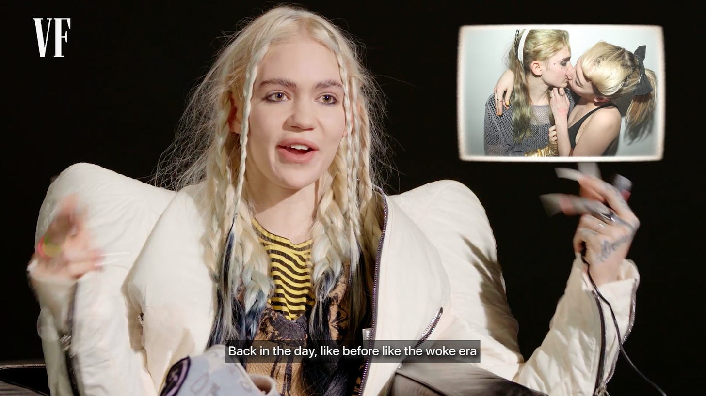 Screenshot of Grimes in a dumb looking jacket with an OTS of her 2012 party kiss picture that she supposedly hacked hipster runoff over, from the Vanity Fair video. The caption reads “Back in the day, like before the woke era”