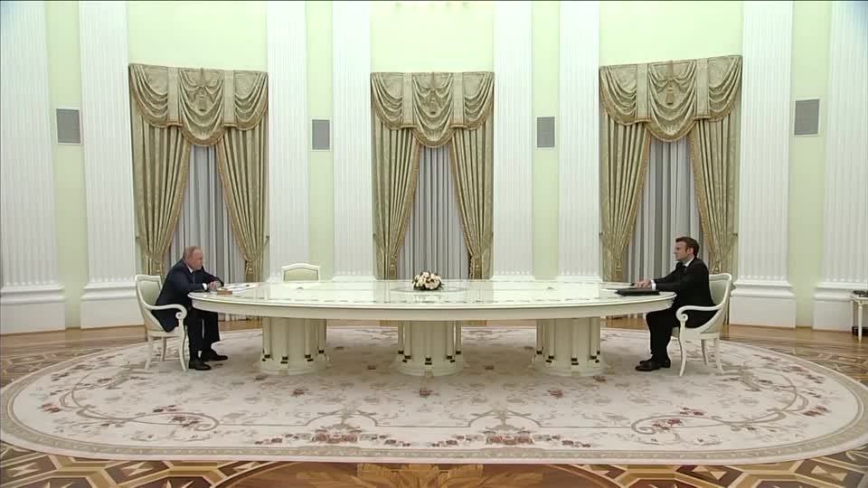 Putin and Macron sitting far apart at a long white table.