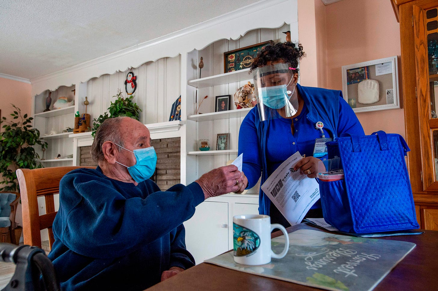 R.N Natalie O'Connor hands a vaccine card to Stanley Mowel (L) before vaccinating him at his home in Manchester, Connecticut on February 12, 2021