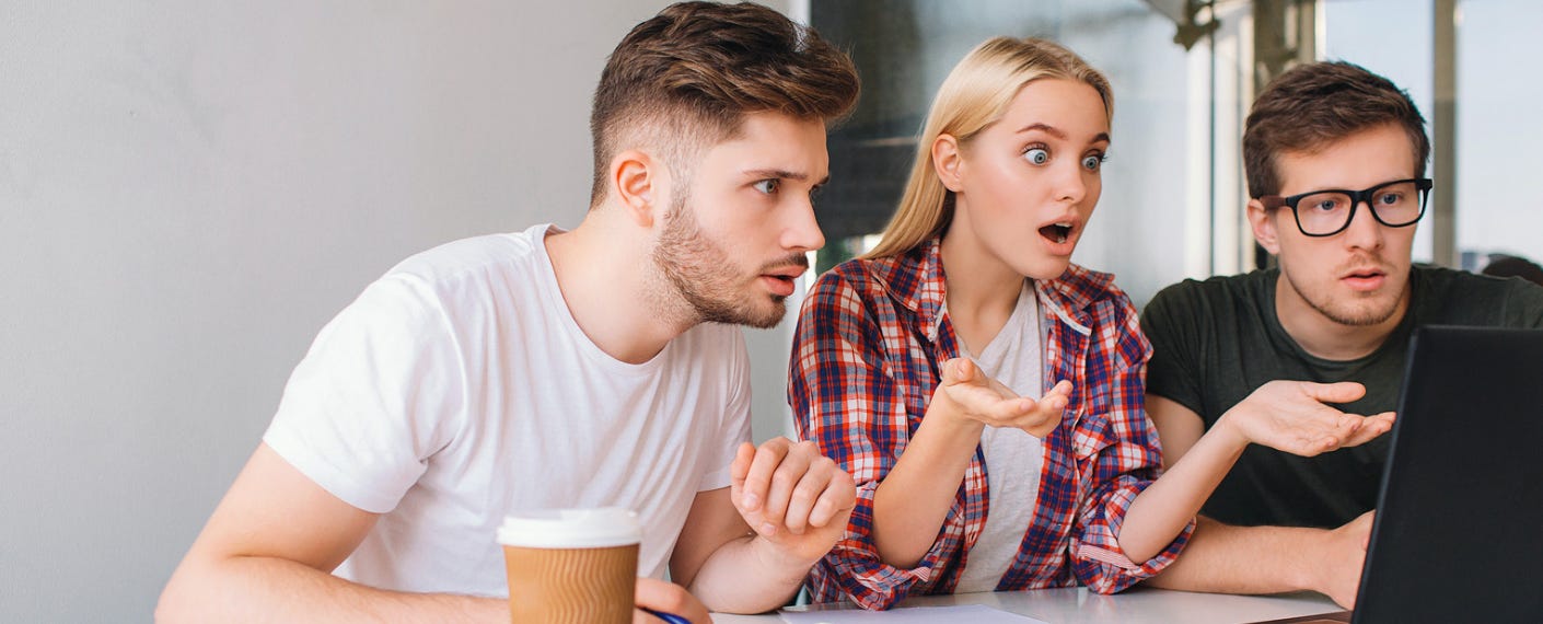 A woman and two guys looking shocked at a laptop