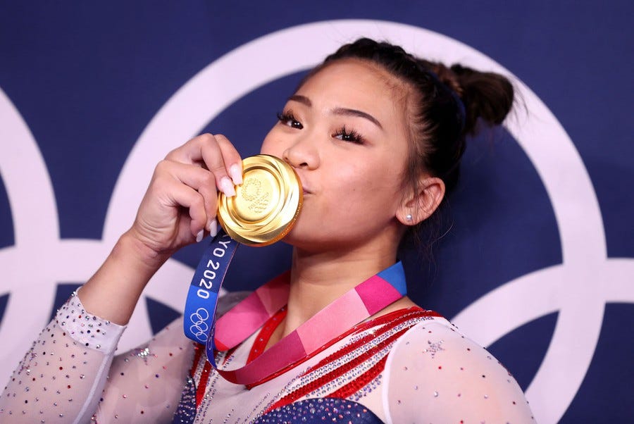 A gymnast kisses her gold medal while posing.