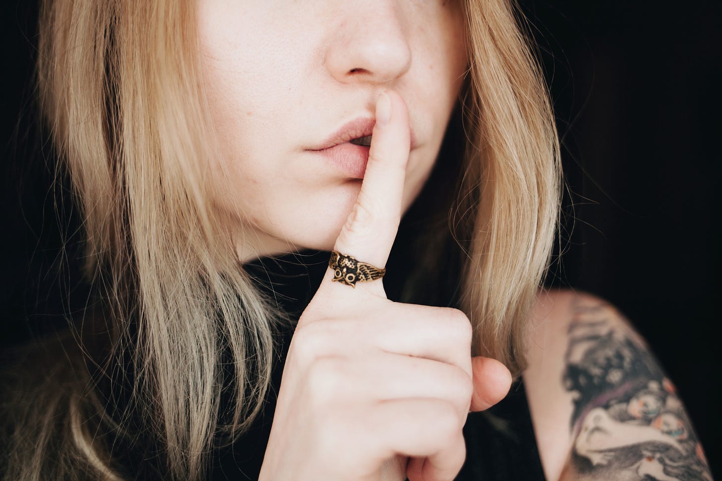 A woman presses her inidex finger to her lips in the universal sign for silence.
