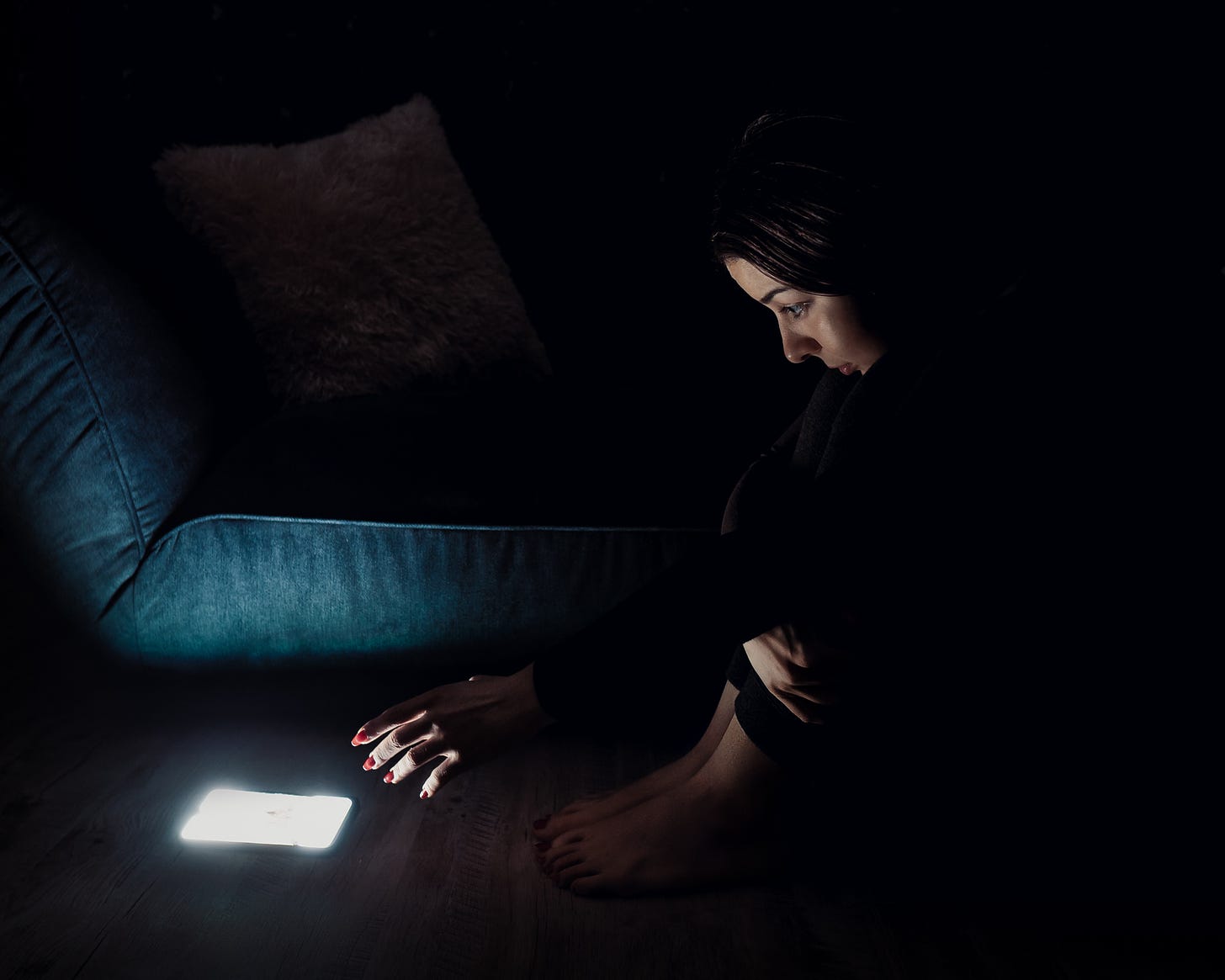 An image of a woman in the dark, reaching for her smartphone