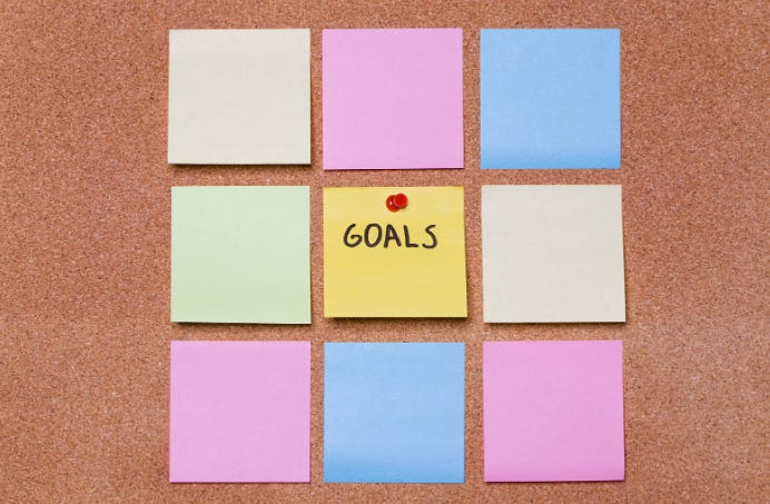 Image of corkboard with blank post-it notes, and one in the middle that says "Goals."