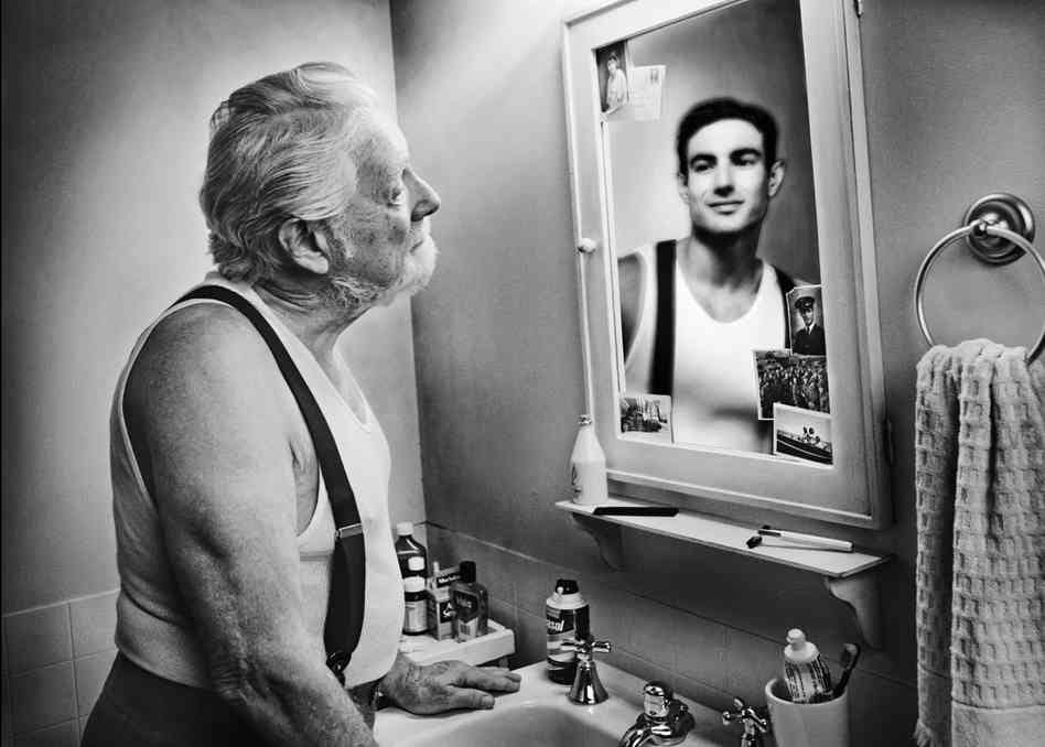 Old man sees reflection in bathroom mirror of his younger self.