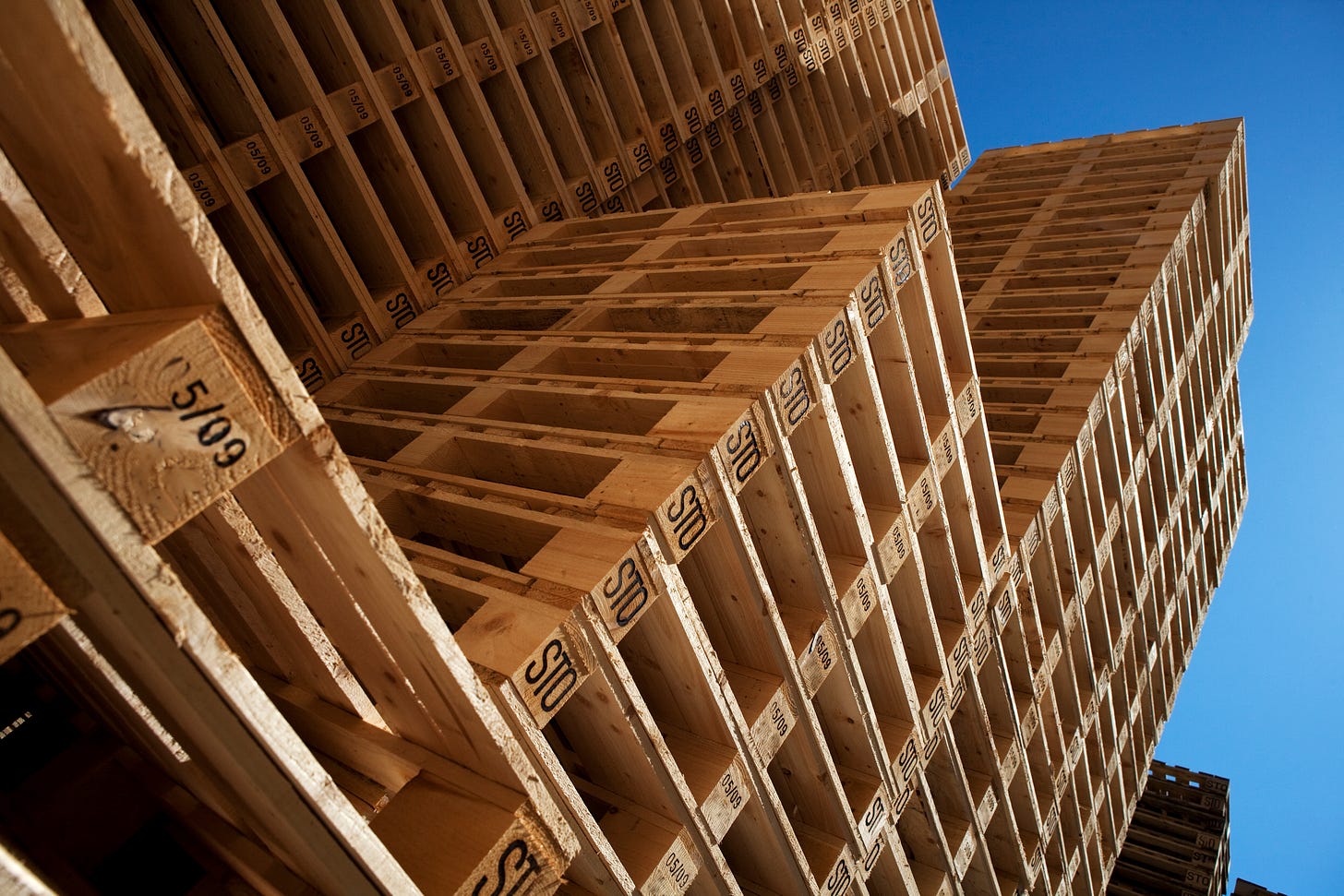 Multilevel stacks of wood pallets under a cloudless blue sky