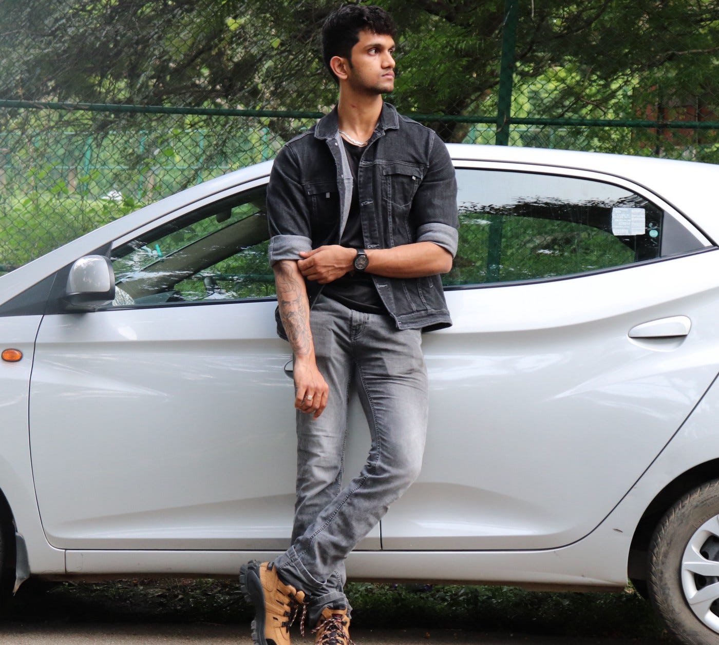 A photo of the author dressed in a jacket and jeans standing against his car’s side