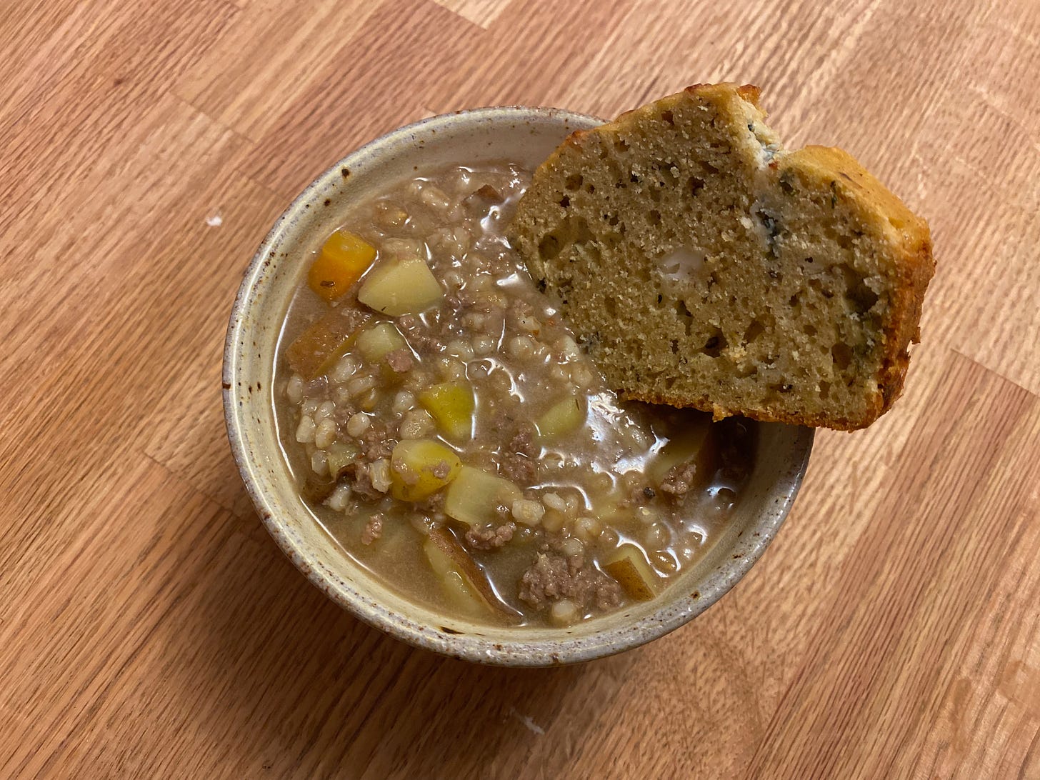 A ceramic bowl of lamb and barley stew with a piece of black pepper quick bread resting on top.