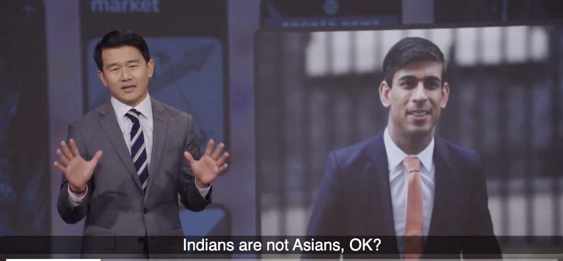 A screenshot of the Daily Show were a Malaysian Chinese man wearing a grey suit stands before a screen that shows a picture of an British Indian man wearing a blue suit. Caption on the bottom of the picture reads: “Indians are not Asians, OK?”