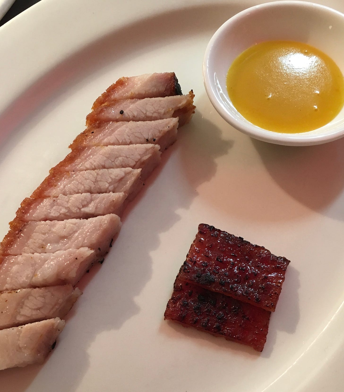 A thick cut of Cantonese crispy pork belly on its side on a white plate, with a serving of mustard sauce in a small white bowl and small portion of crispy belly skin, crisp-side up