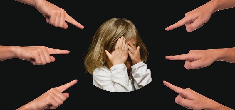 Picture of six fingers pointing to a child with hands covering her face as to protect herself from the pointing fingers.