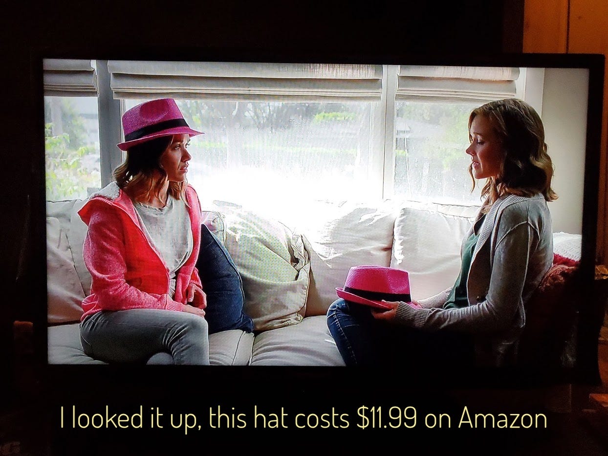 Annie, wearing a hot pink fedora with a black hat band, talking to a woman holding that very same hat, captioned "I looked it up, this hat costs $11.99 on Amazon"