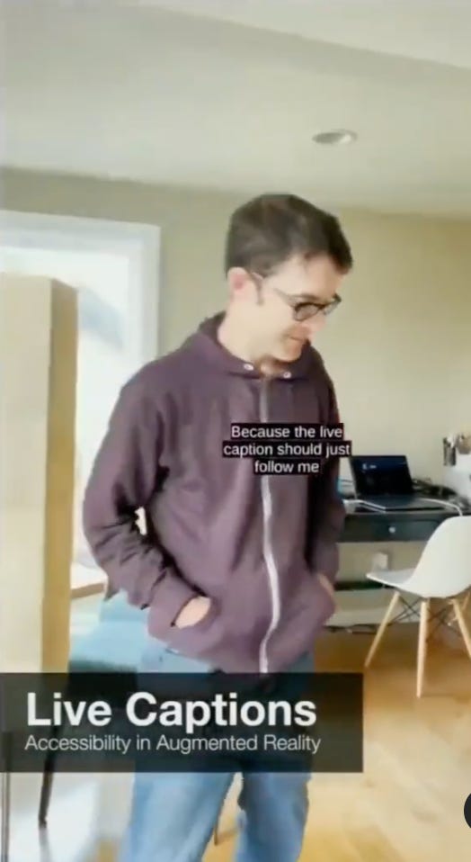 Man in hoodie and jeans, standing in room with captions on top of the screen