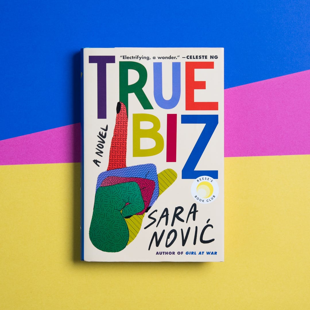 ID: Tan book cover with multicolored letters spelling out “True Biz” and a multicolored hand in a “d” handshape on the left side, with “Sara Novic” on the bottom right and a yellow and white Reese’s Book Club sticker above that.