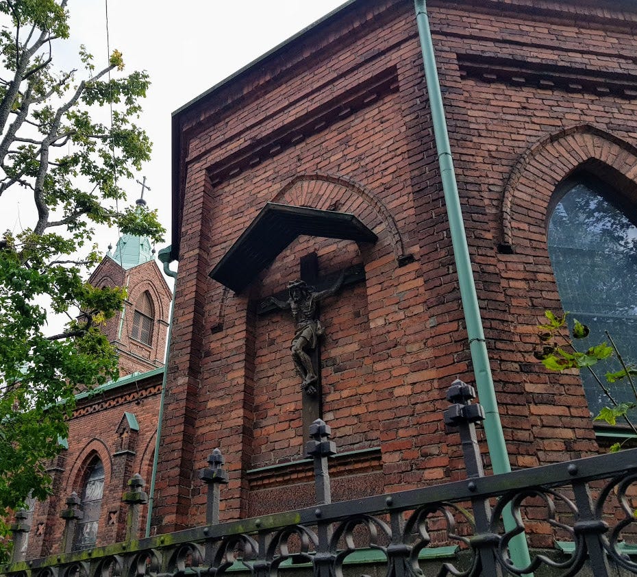 Ett krucifix på ytterväggen till en kyrka i röd tegelsten.