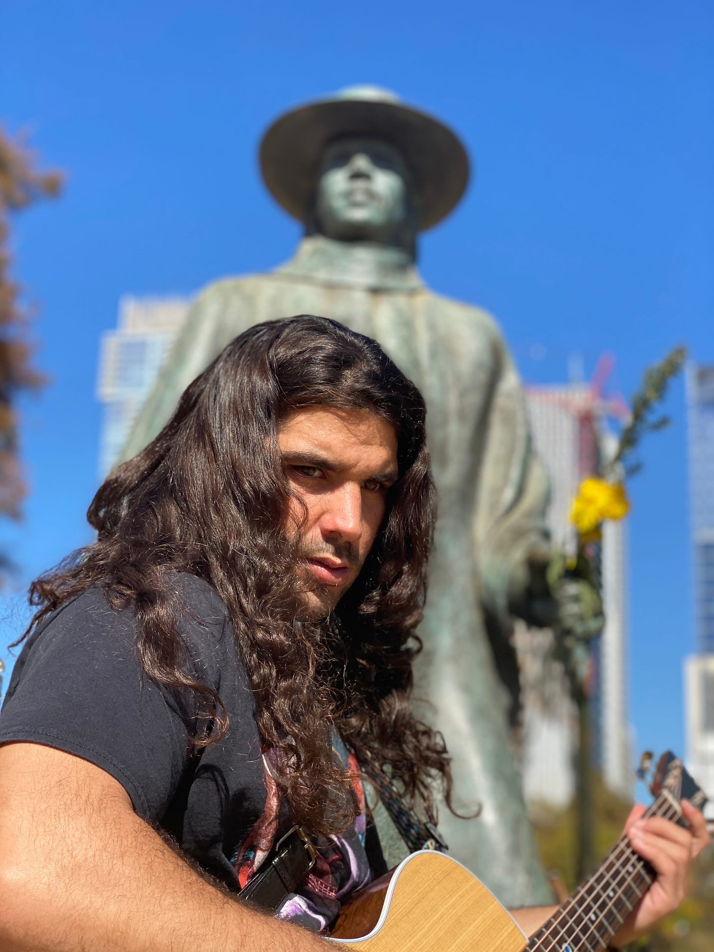 anthony standing so serious with his hear down and shining so beautifully and statue of stevie ray vaughn is behind his head blurred out