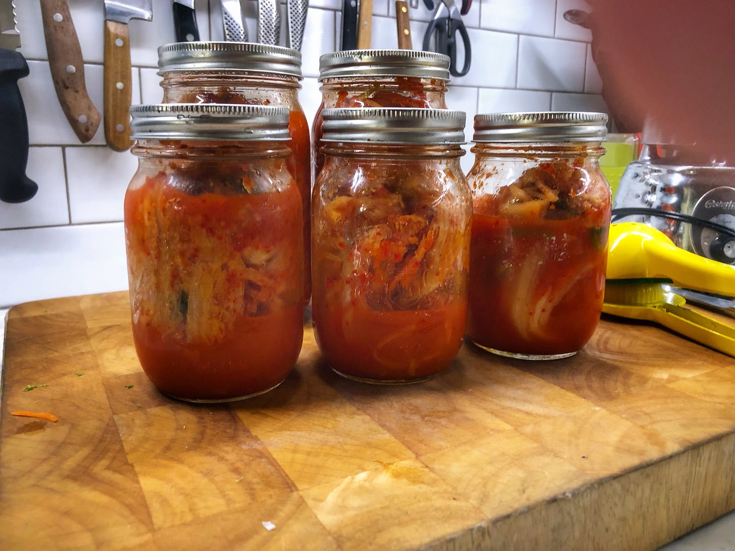 Five jars of kimchi on a cutting board. My fingertip is covering part of the camera lens.