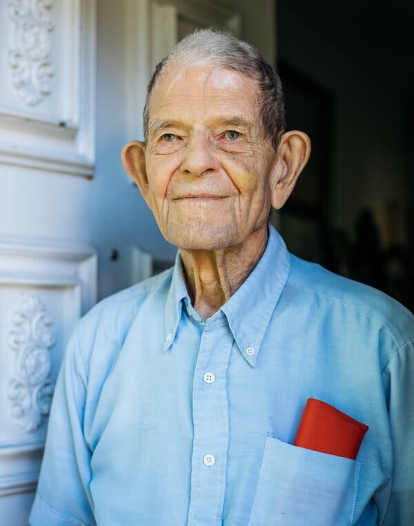 Staughton Lynd as an older man. He is wearing a blue button down shirt and standing in a doorway.