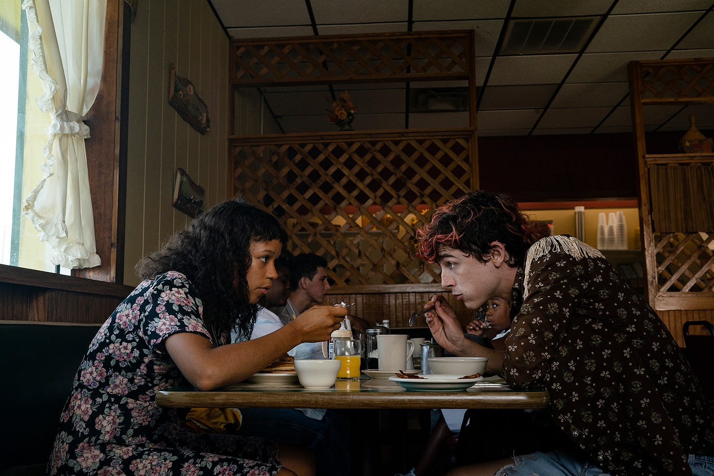BONES AND ALL film still picturing Taylor Russell and Timothée Chalamet eating at a diner table.