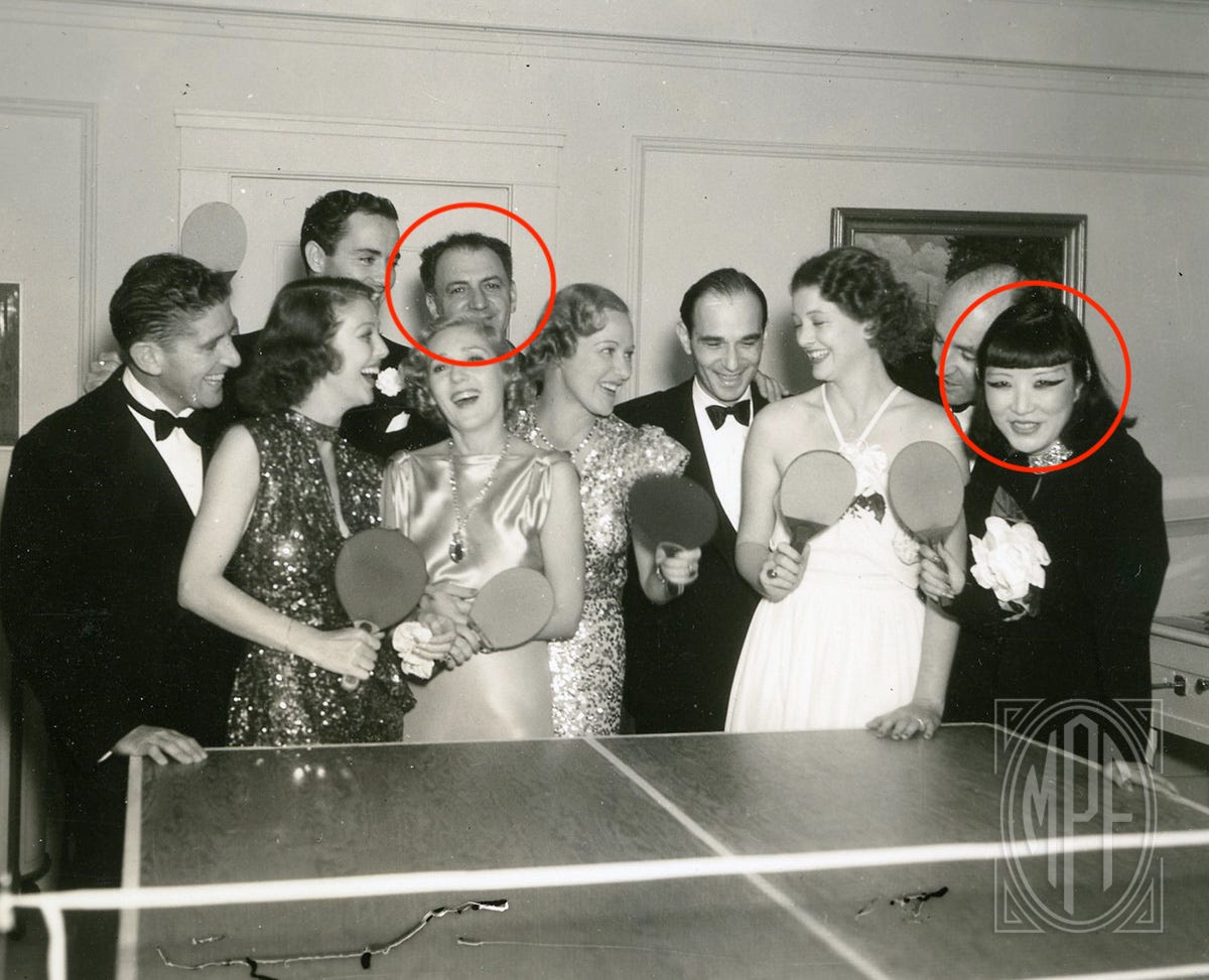 The Mary Pickford Foundation photo of Mary Pickford and a group of friends partying around the ping-pong table at Pickfair circa 1935; red circles identify Harry Lachman and Jue Quon Tai.