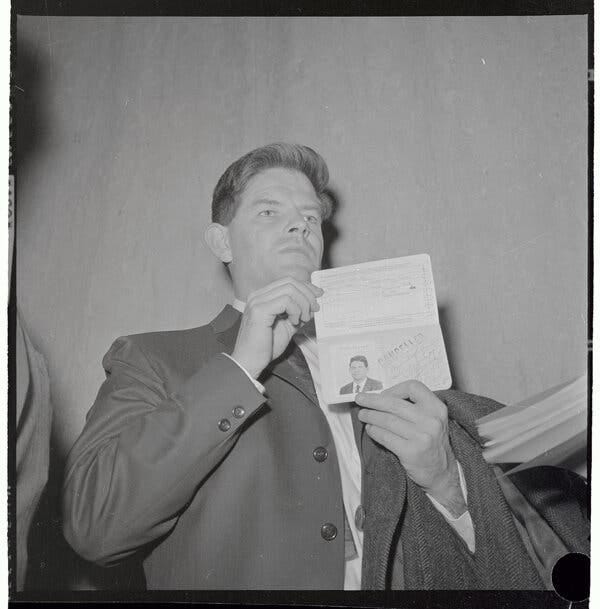 Mr. Lind, looking angry, holds up his passport, which is marked CANCELED.