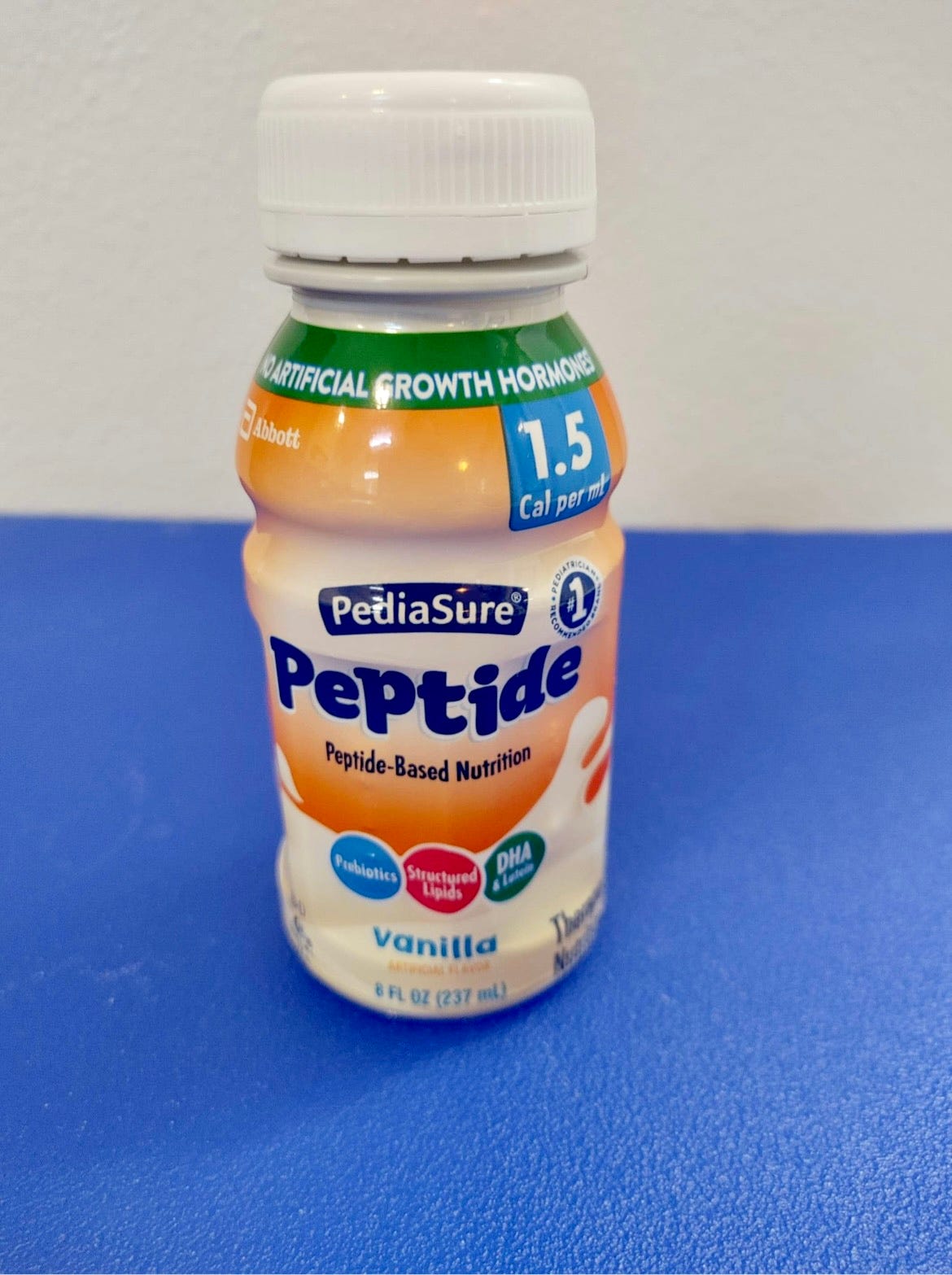 A close-up of an orange bottle of Abbott Laboratories' Pediasure Peptide 1.5 cal formula on a blue tabletop. 