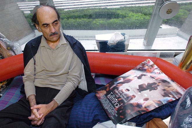 (FILES) In this file photo taken on August 12, 2004 Mehran Karimi Nasseri looks at a poster of the movie inspired by his life, in the terminal 1 of Paris Charles De Gaulle airport. - Mehran Karimi Nasseri, a political refugee who lived over 18 years in Paris' Roissy-Charles de Gaulle airport and inspired director Steven Spielberg's "The Terminal", died, aged 77, at Roissy-Charles de Gaulle airport's terminal 2F, as reported to AFP by airport officials.