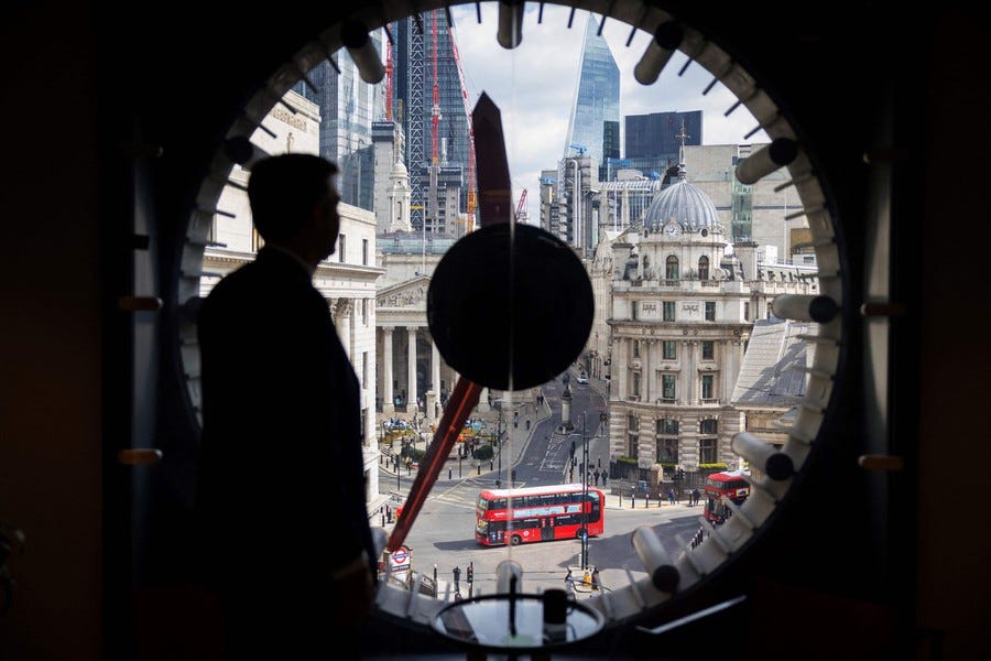 A man looks at downtown London, seen through a round window that is also a clock face.