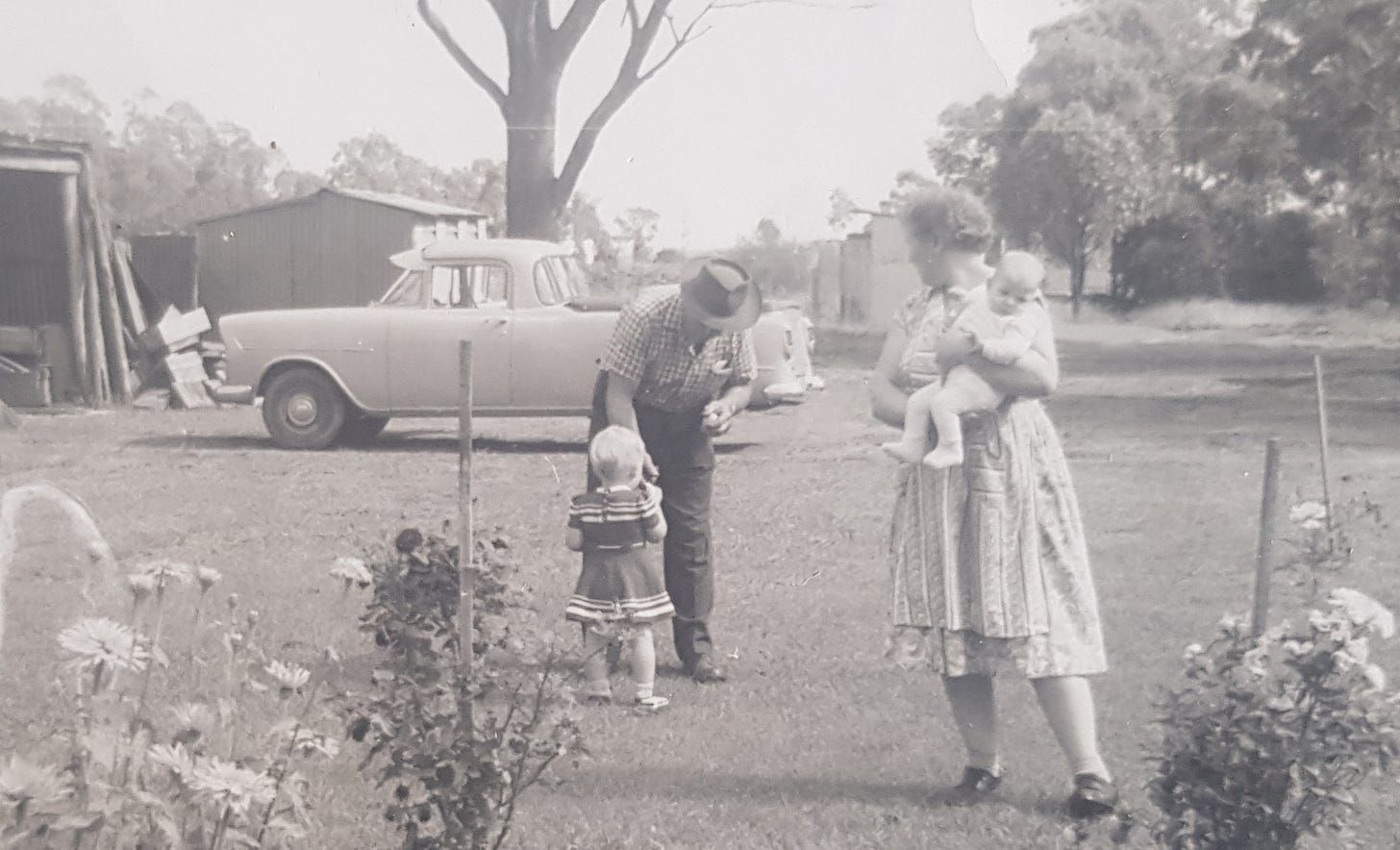 Black and white photo from 1961, grandfather wearing hat, grandmother wearing apron, toddler, baby, utility vehicle